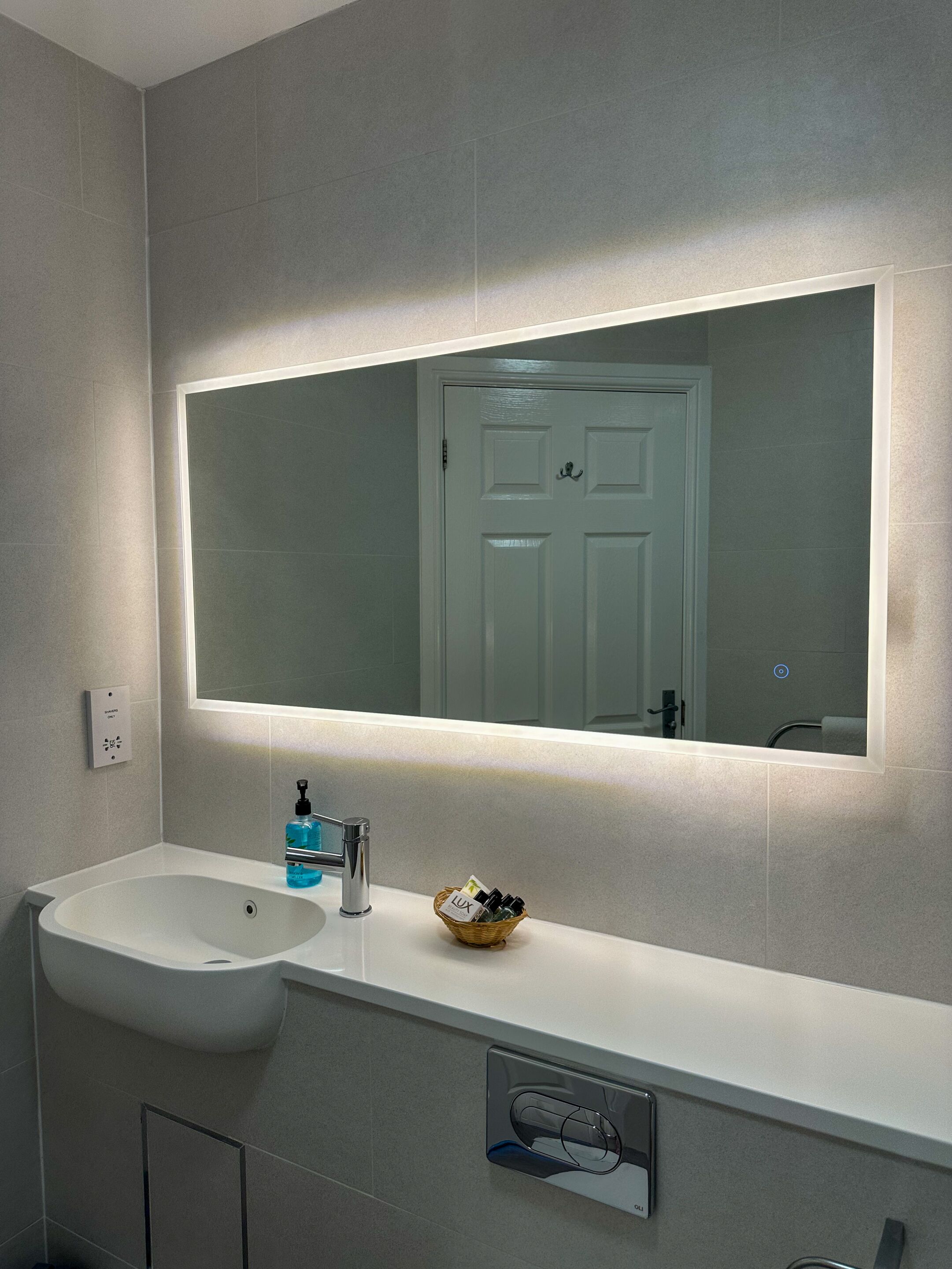 Un baño con lavamanos blanco, un espejo grande y una lámpara en la pared.