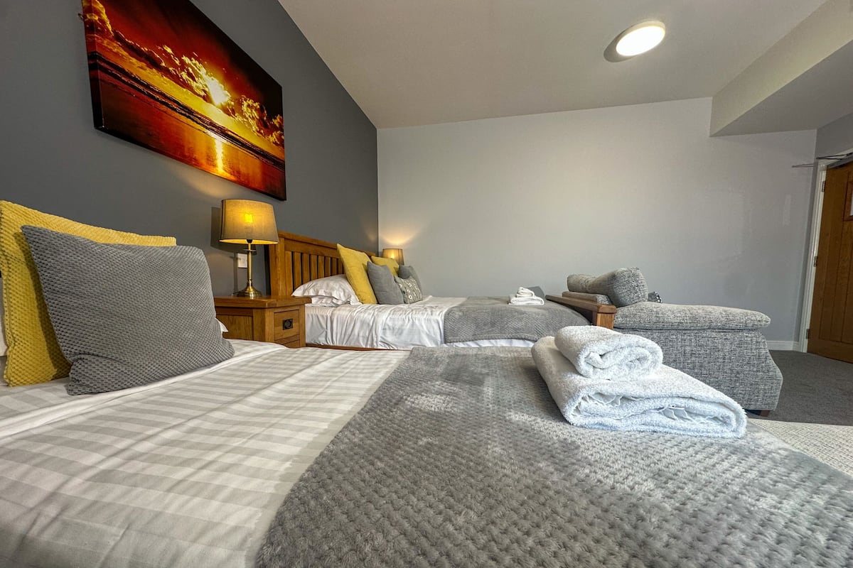 Ein Hotelzimmer mit zwei Betten, einem Nachttisch mit Lampe, einem Sessel und einem Bild an der Wand.