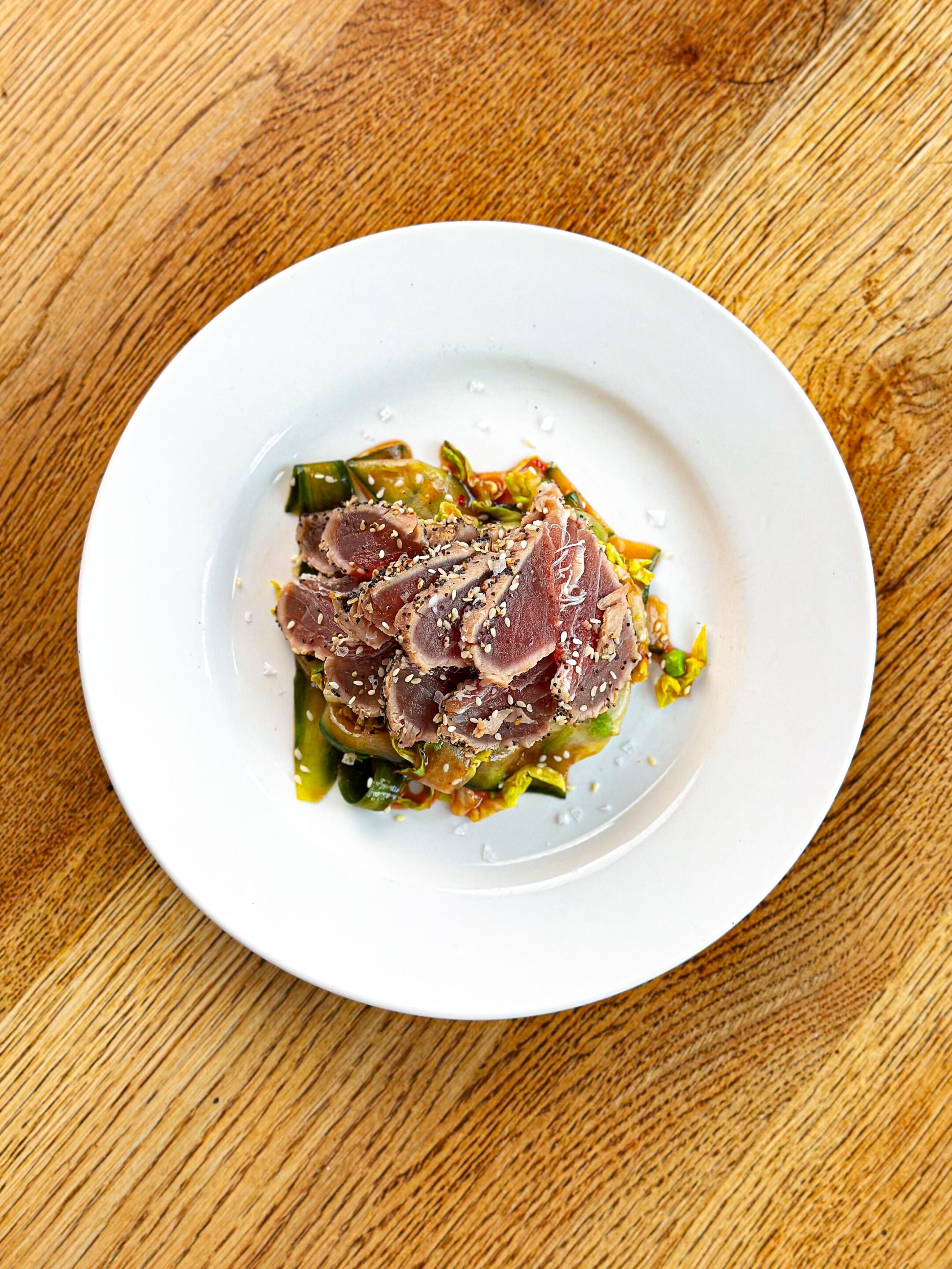 Ein weißer Teller mit geschnittenem Fleisch und Gemüse auf einem Holztisch.