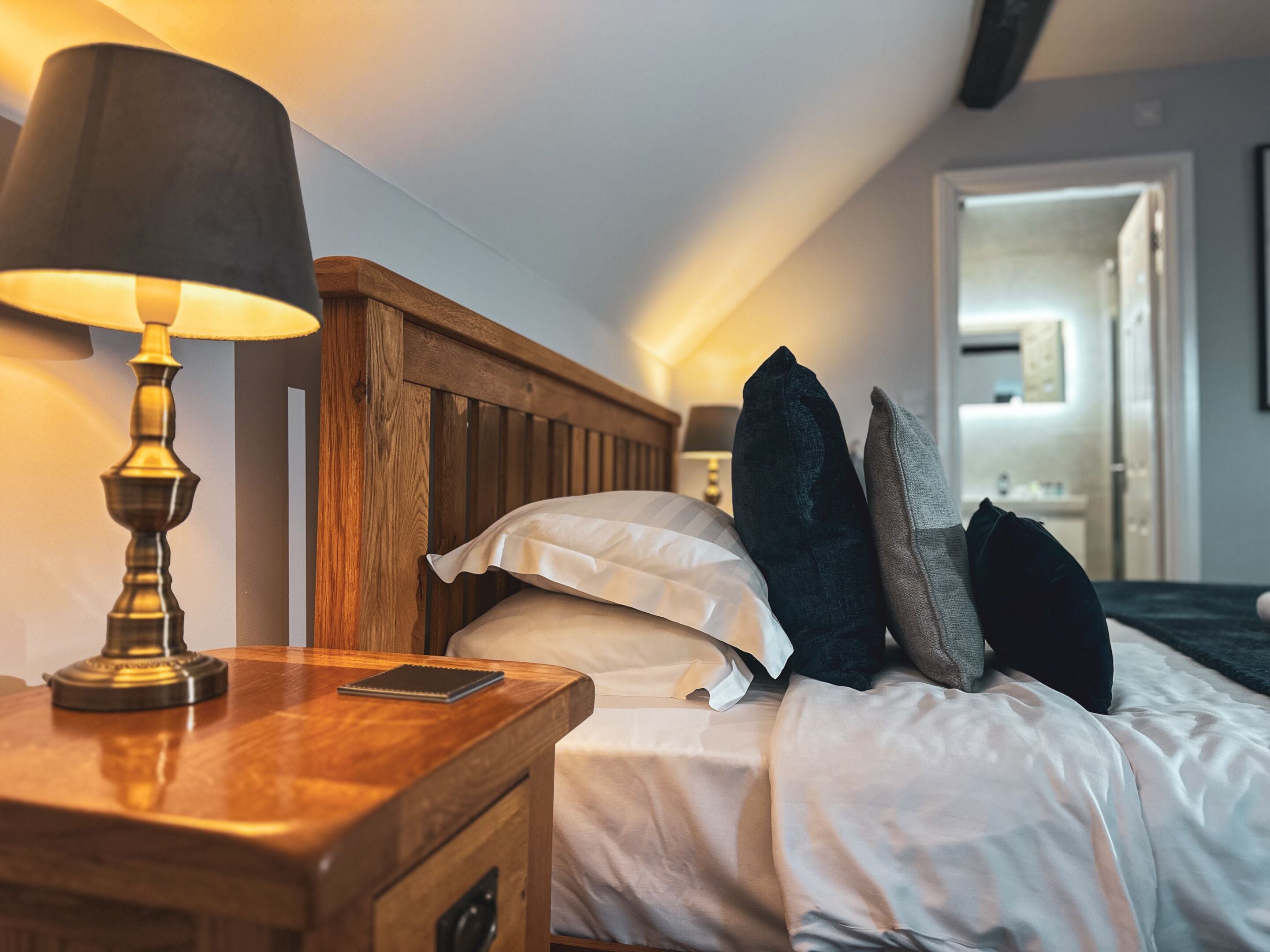 Una cama bien hecha con sábanas blancas, un cabecero de madera y una lámpara de noche.