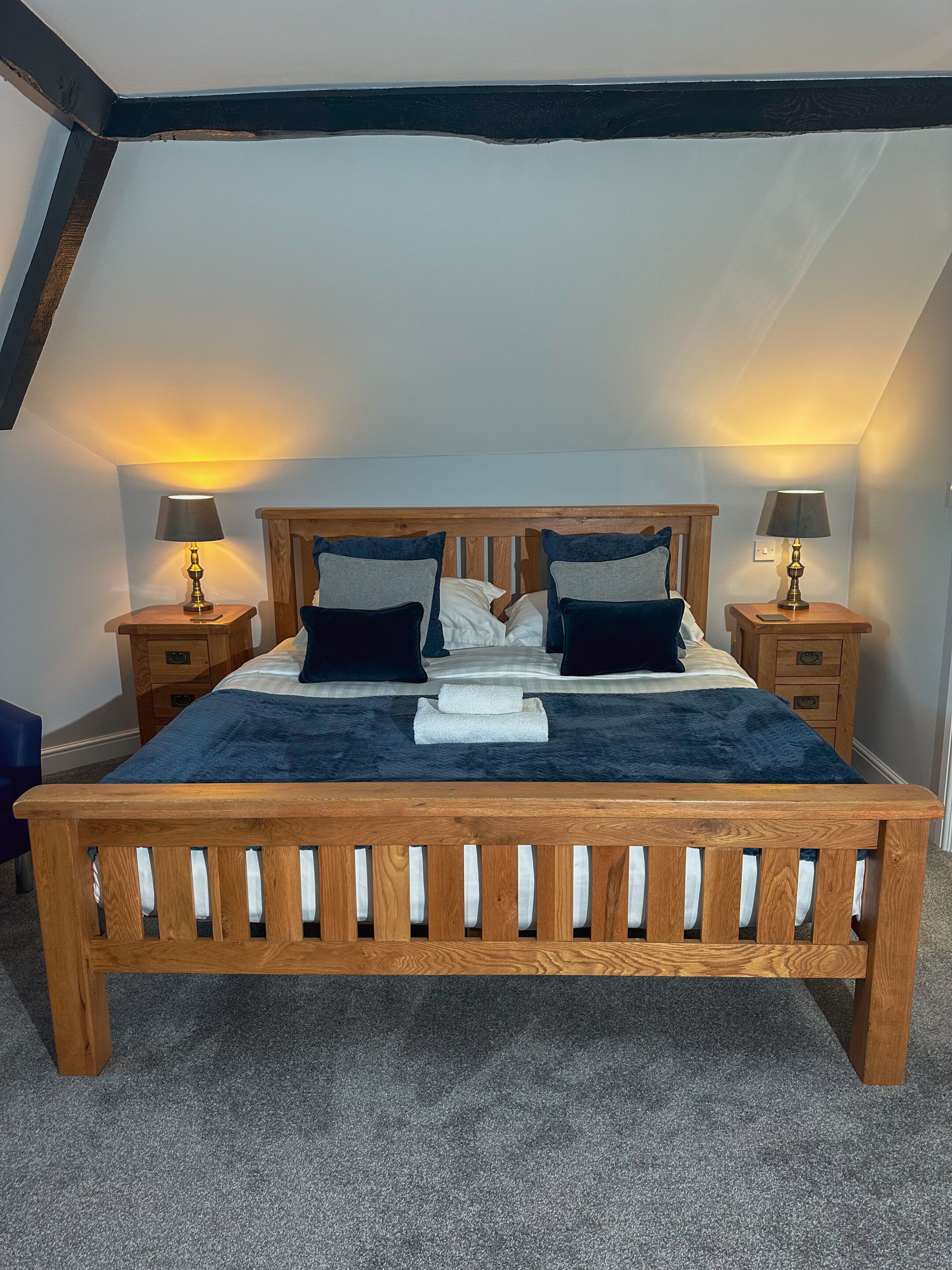 A bedroom with a wooden bed, two bedside tables with lamps, a blue headboard, and a sloped ceiling.
