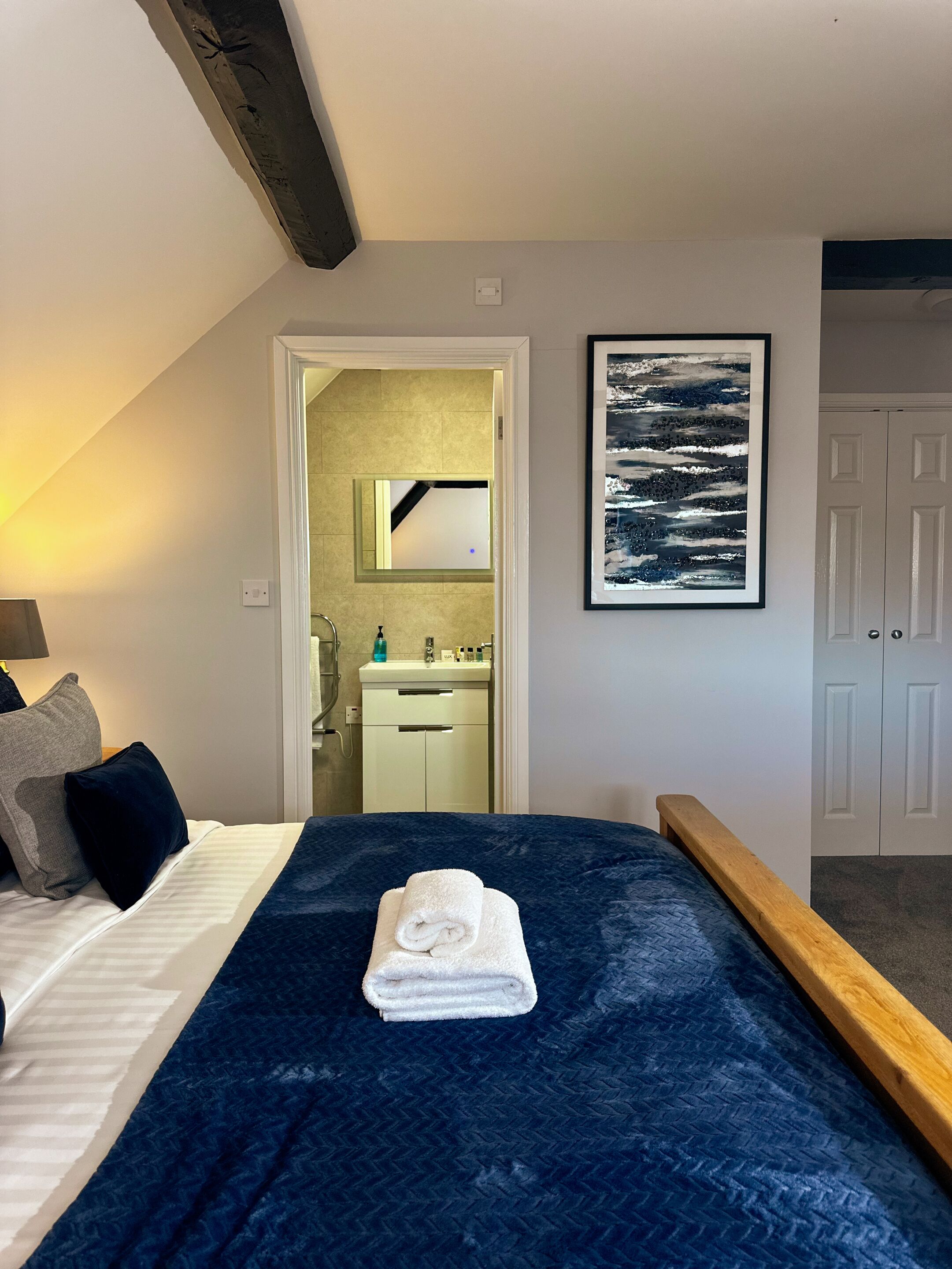 A bedroom with a bed, a bathroom visible through an open door, and a framed picture on the wall.