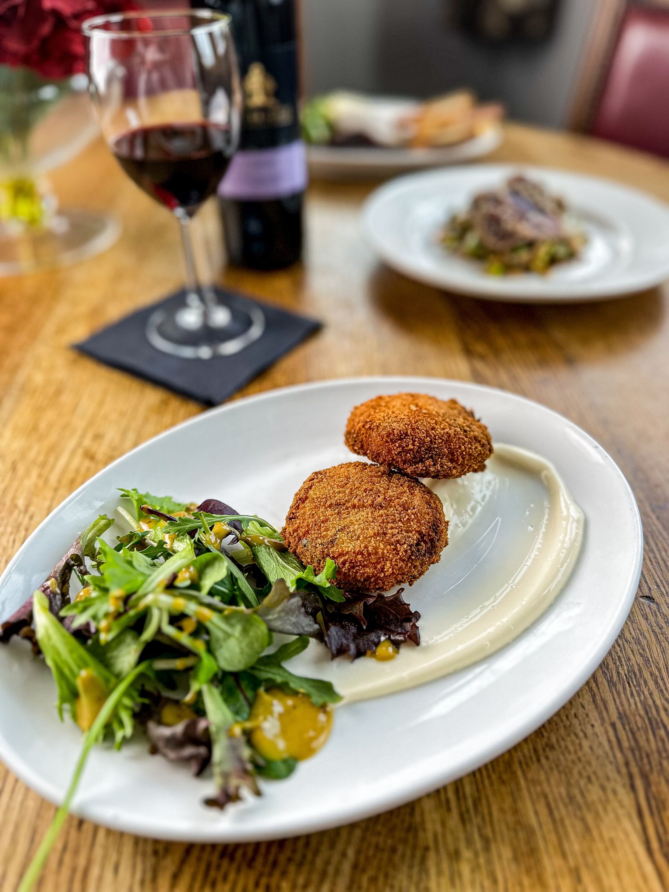 A plate with two breaded items and a salad on a wooden table.