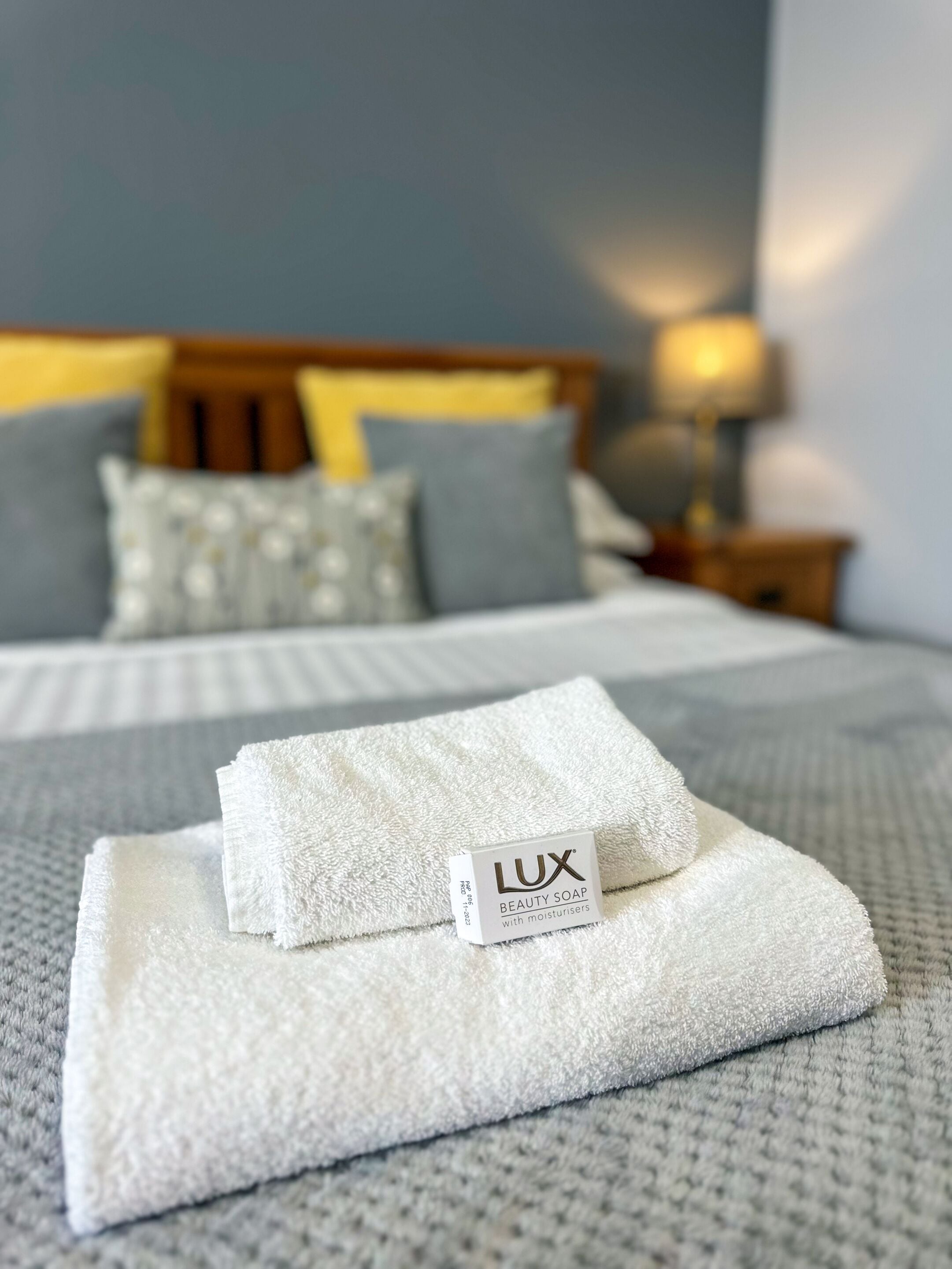 Un lit bien fait, avec une couette blanche et une serviette blanche pliée, sur laquelle on peut voir une étiquette du savon de beauté Lux.