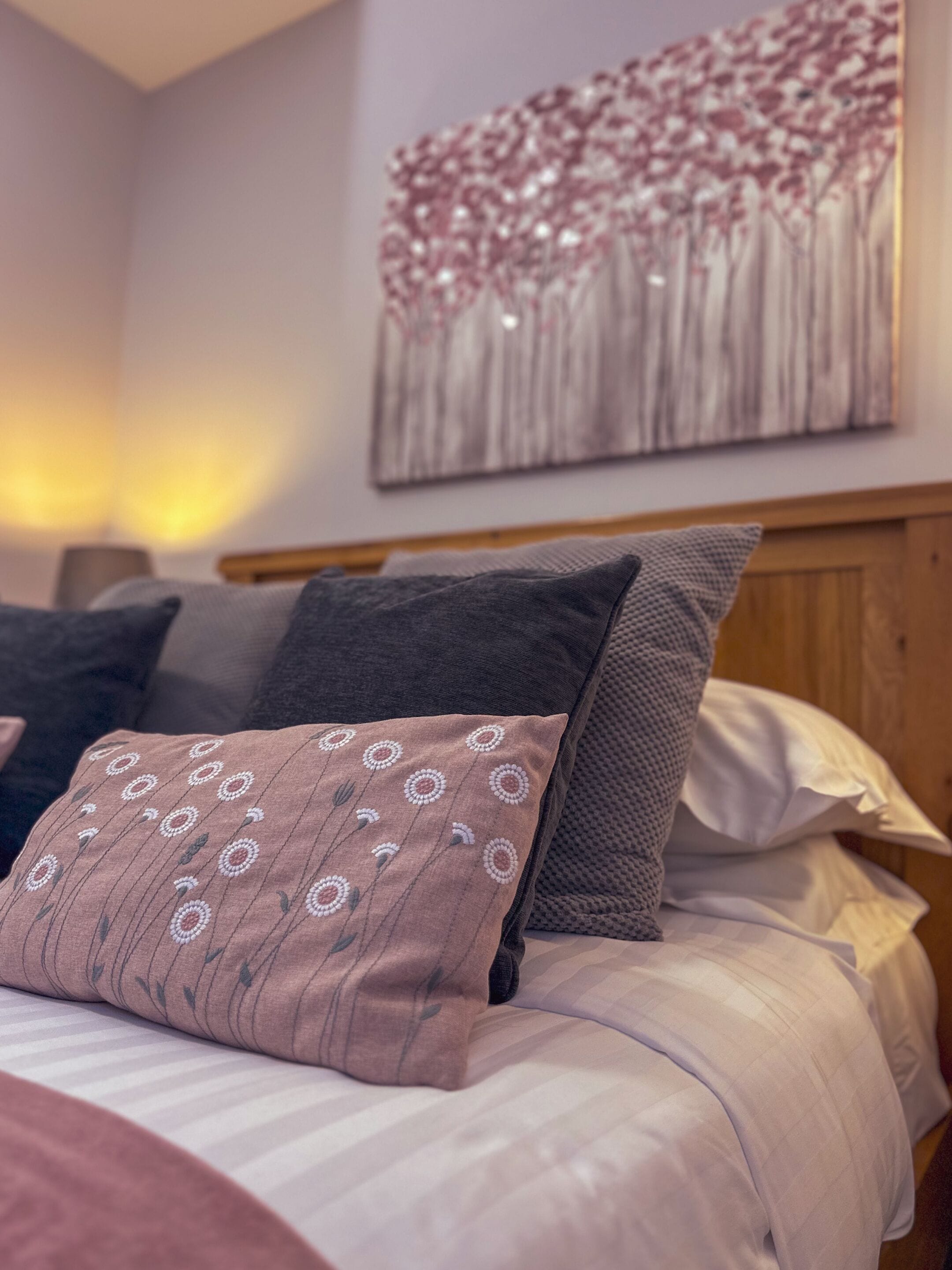 A neatly made bed with a patterned pillow and a wall painting.