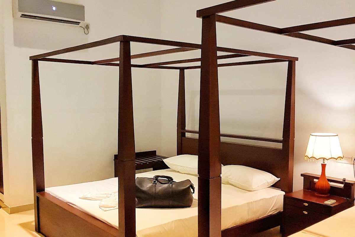 A four-poster bed with a wooden frame, a bedside table with a lamp, and a wall-mounted air conditioning unit.