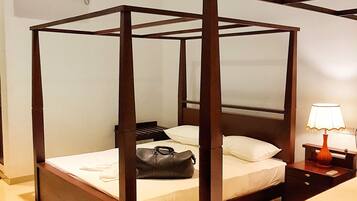 A four-poster bed with a wooden frame, a bedside table with a lamp, and a wall-mounted air conditioning unit.