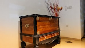 Un aparador de madera con detalles metálicos ornamentales, colocado frente a una pared lisa con una planta decorativa.