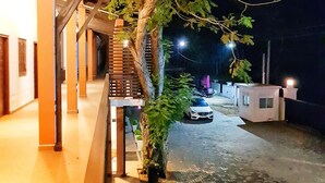 Un espacio al aire libre cubierto con un árbol, un coche estacionado al fondo y un edificio con techo inclinado.