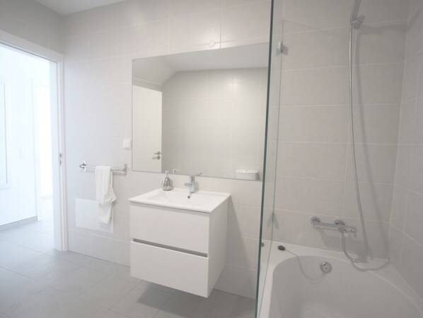 Un baño moderno con ducha envuelta en vidrio, un lavabo blanco y un espejo sobre él.