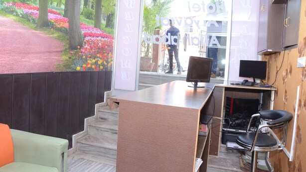 Un mostrador de recepción con una computadora, una silla y una escalera que lleva a una puerta con un cartel de 'Welcome'.