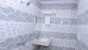 Un baño con pared de azulejos estampados, un lavamanos, un espejo, un perchero para toallas y un cabezal de ducha.
