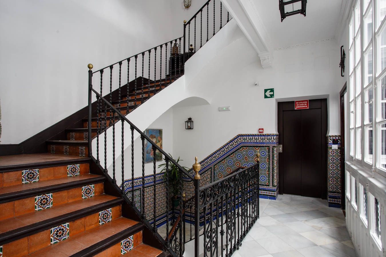 Una escalera con barandillas decoradas y baldosas estampadas, que conduce a un piso superior.