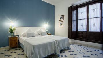 Un dormitorio con dos camas, una mesita de noche con un jarrón de flores y una ventana con cortinas.