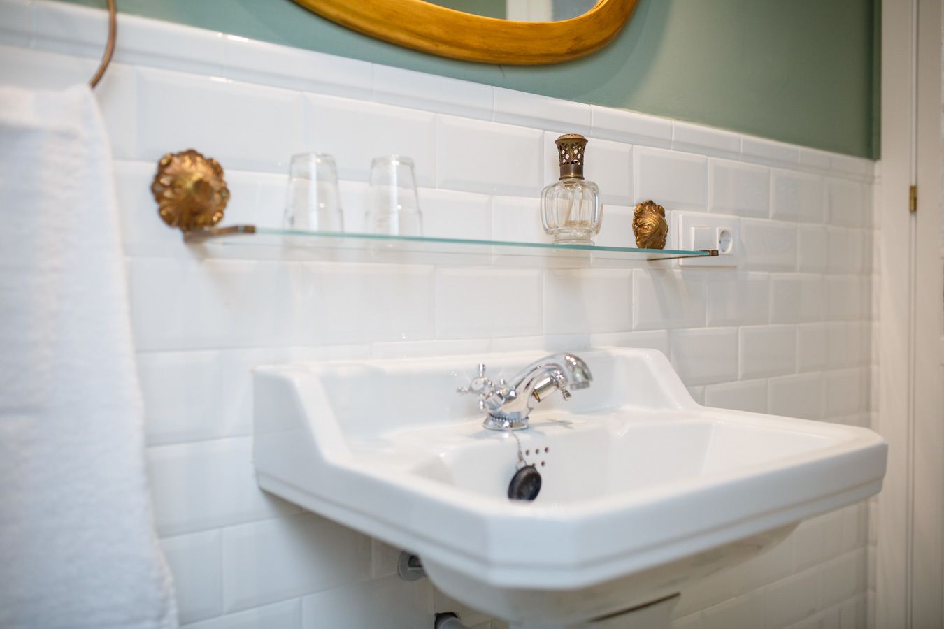 A bathroom with a white sink, a mirror, and a glass shelf with toiletries.