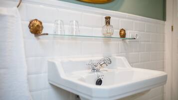 A bathroom with a white sink, a mirror, and a glass shelf with toiletries.