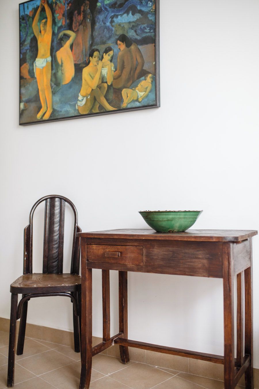 Ein Zimmer mit einem Holzstuhl, einem Tisch mit einer grünen Schüssel und einem Bild an der Wand.