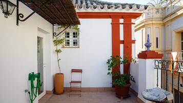 Une cour avec un toit en tuiles, une colonne rouge, des plantes en pot, une petite table et une chaise verte.