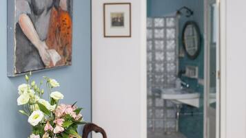 A dining area with a table, chairs, a vase with flowers, a painting on the wall, and a hallway leading to a bathroom.