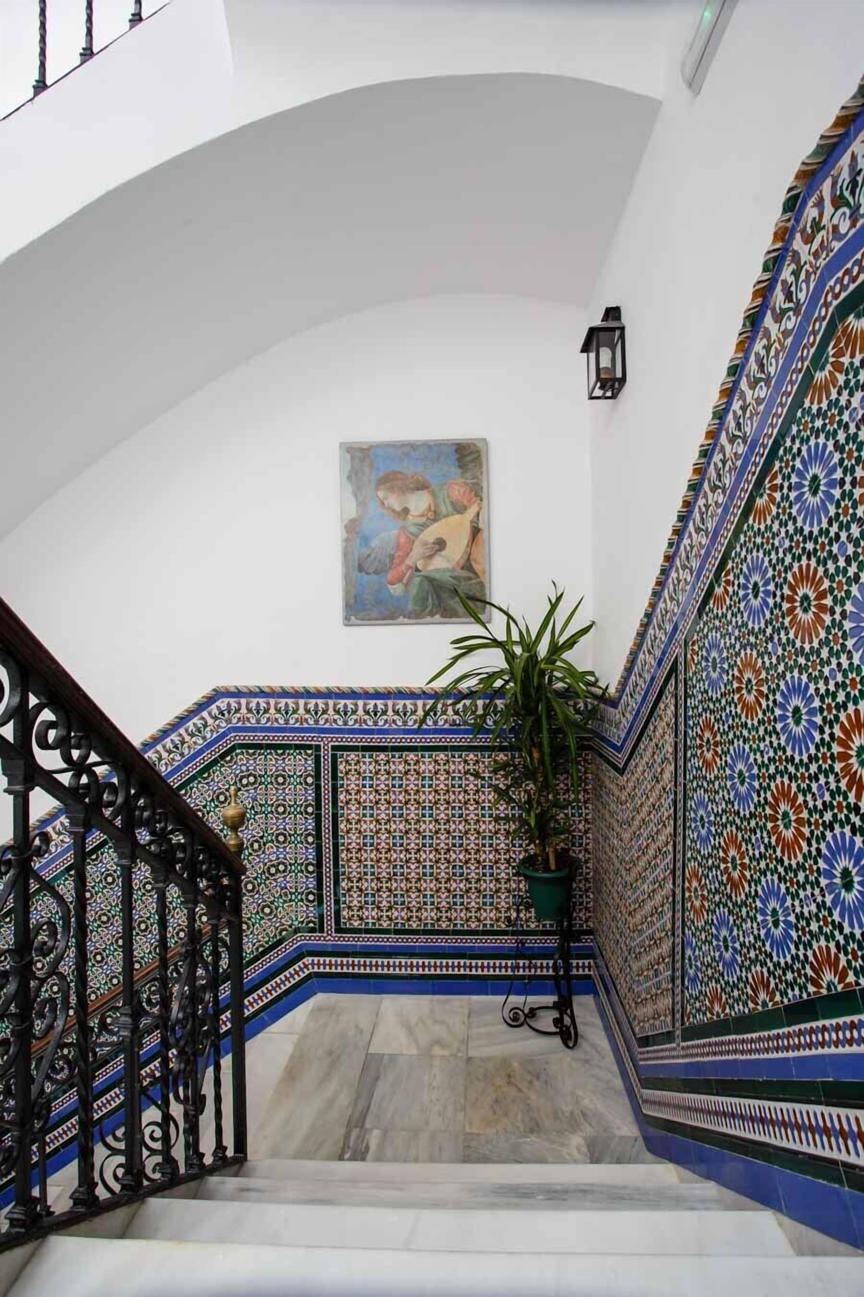A staircase with ornate tile patterns, a potted plant, and a painting on the wall.