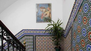 A staircase with ornate tile patterns, a potted plant, and a painting on the wall.