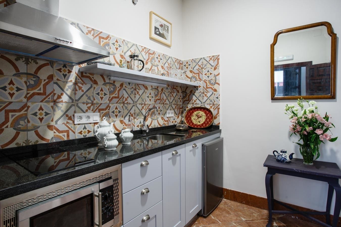 A kitchen with patterned backsplash, stainless steel appliances, and a small table with a vase of flowers.