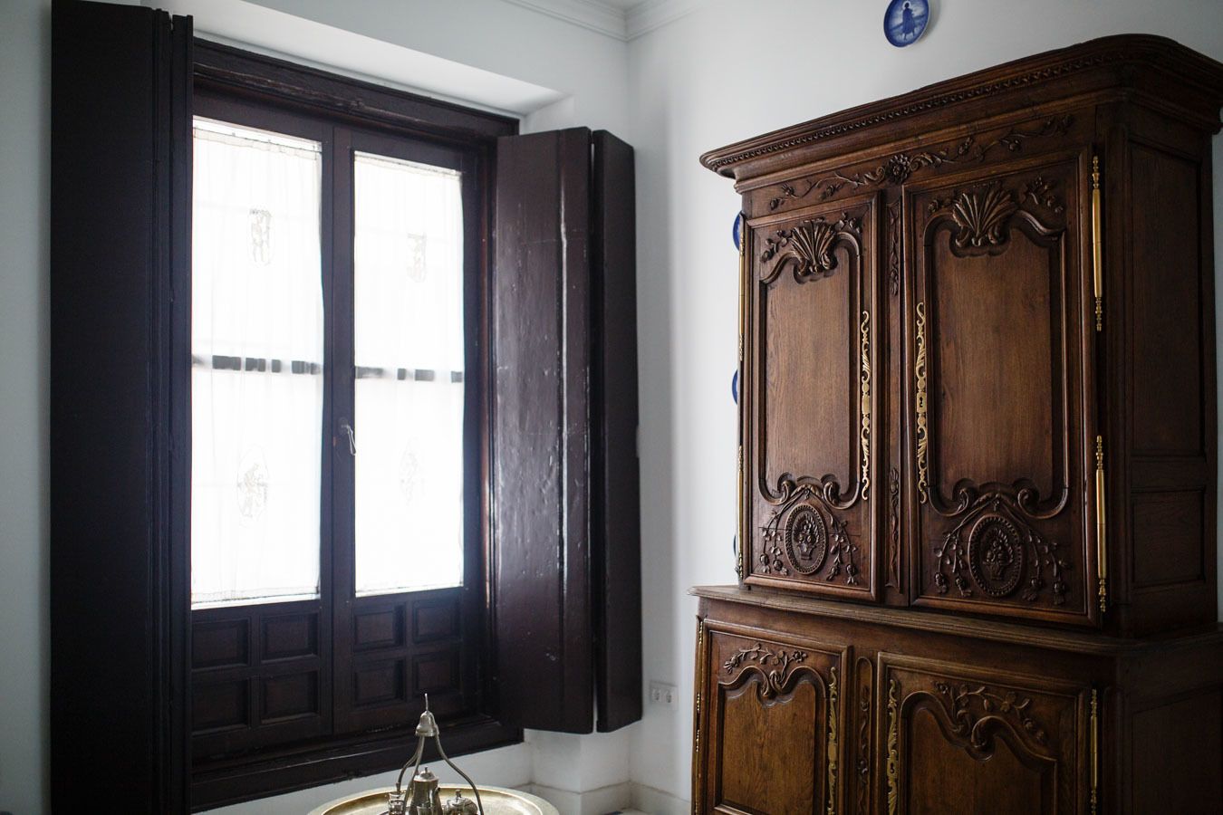 A room with a large window, a wooden cabinet, and a small table with a lamp.