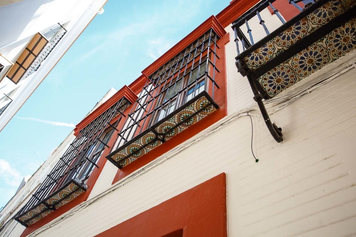 Um edifício com fachada branca e detalhes vermelhos, com grades de janela ornamentadas e um desenho de azulejos perto das janelas.
