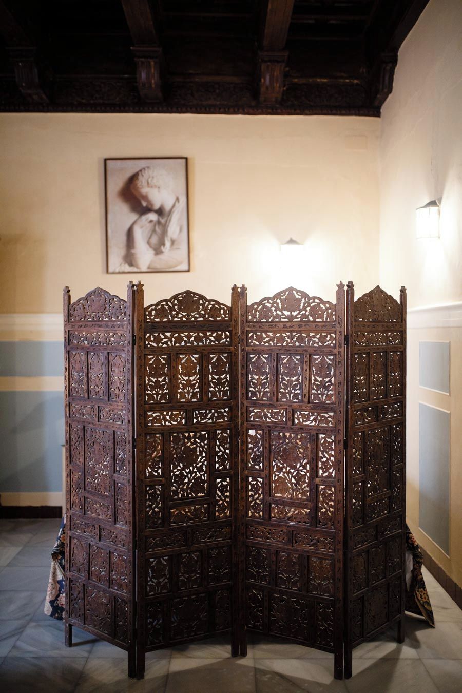 A traditional wooden partition with intricate carvings, a framed artwork on the wall, and a light fixture above.