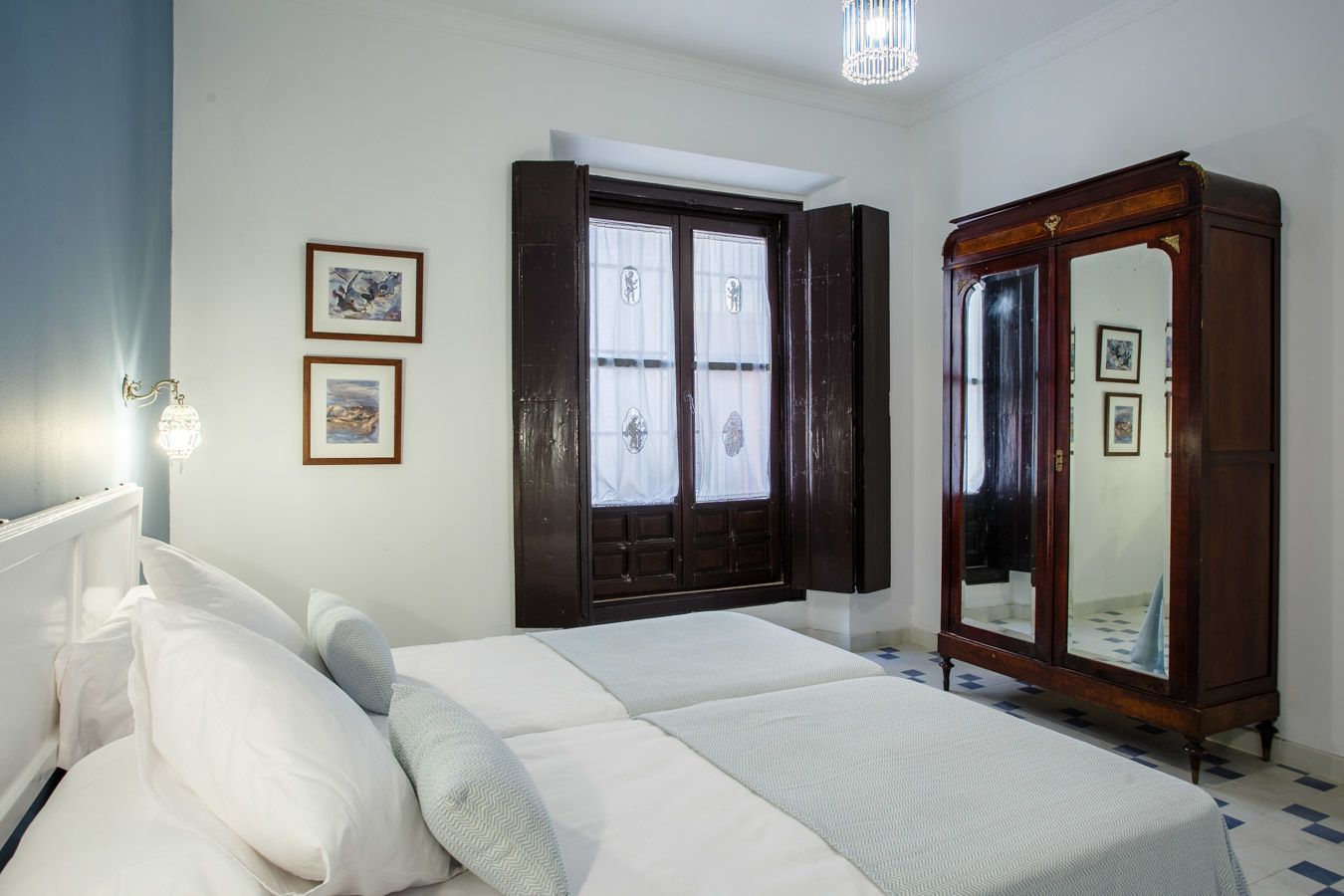 Une chambre à coucher comprenant un lit, une armoire, une fenêtre avec des volets et des lampes fixées au mur.