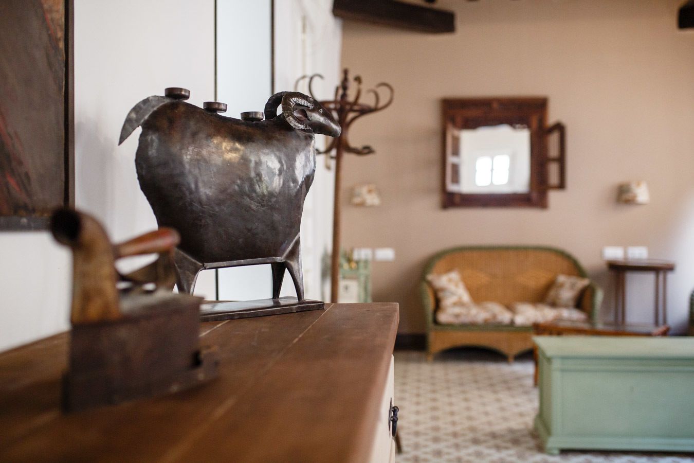 A rustic interior with a wooden table, a decorative metal sculpture, a green sofa, and a mirror on the wall.