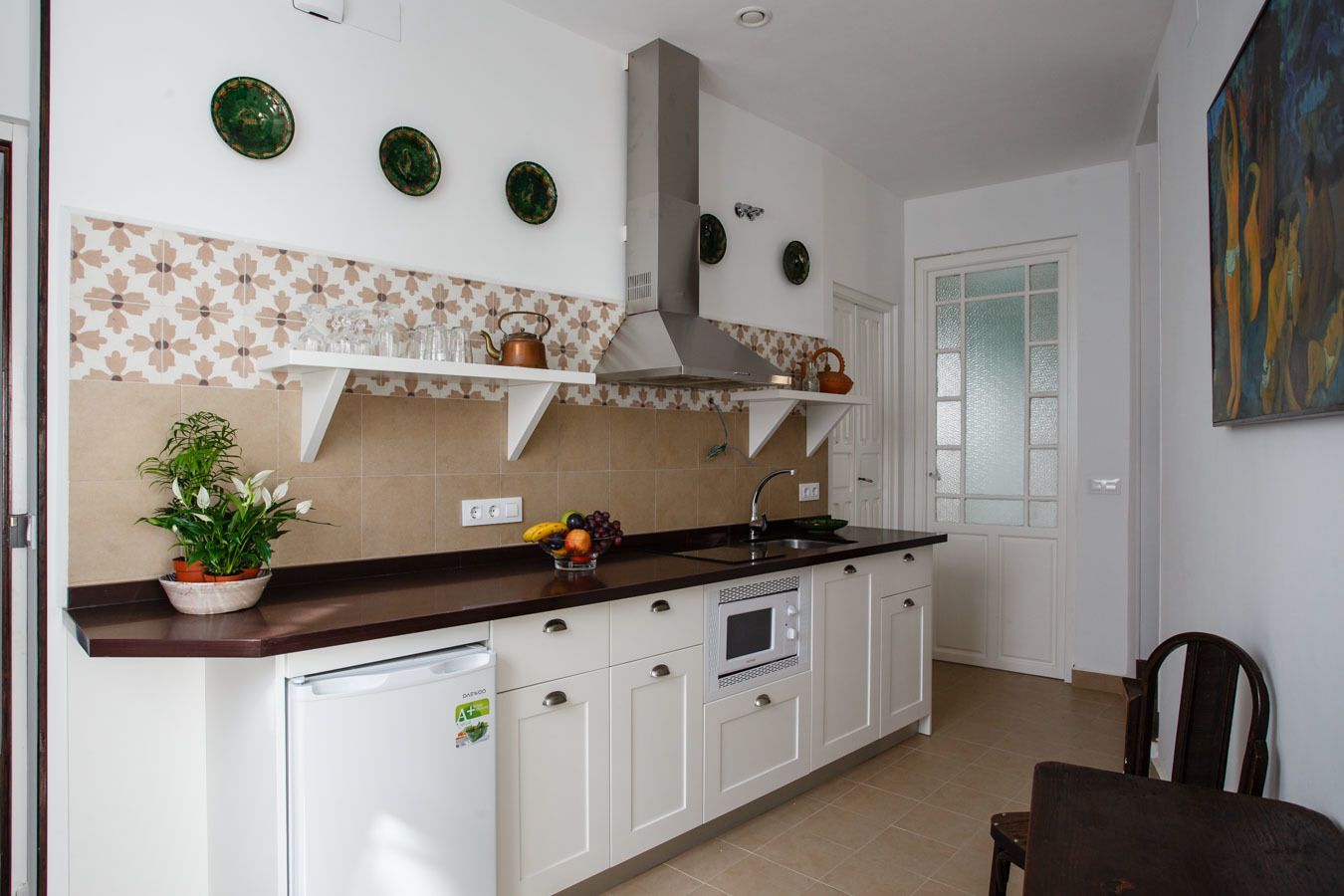 A kitchen with white cabinets, a built-in oven, a microwave, a sink, and a potted plant.