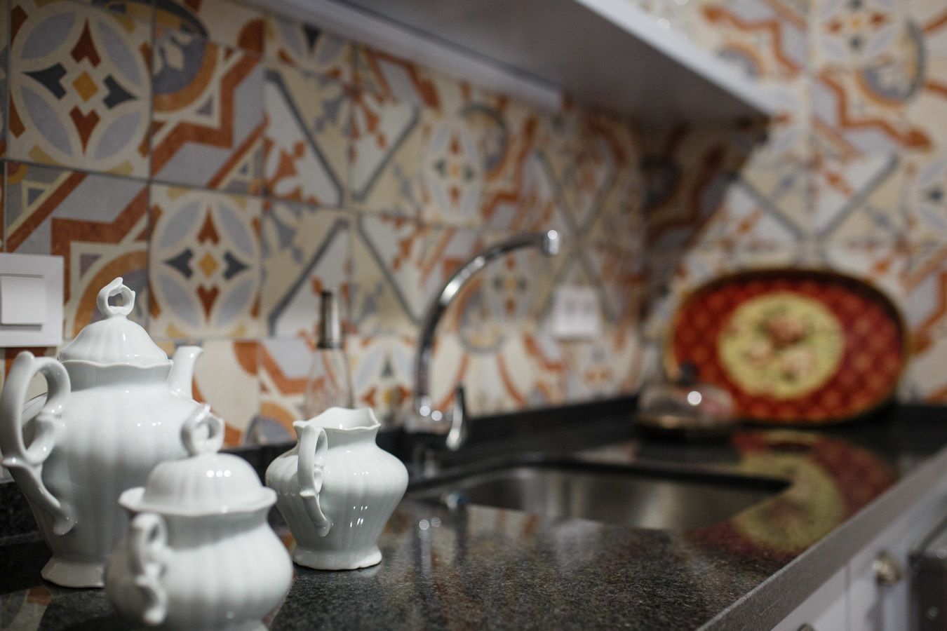 A kitchen with a tiled backsplash, a sink, and white ceramic tea pots.
