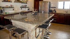 Cozinha moderna com ilha central, eletrodomésticos de aço inoxidável e banquetas de bar.