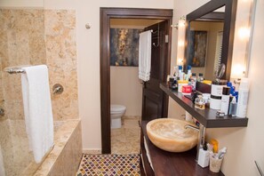 A bathroom with a marble floor, a wooden vanity with a large sink, and toiletries on the counter.