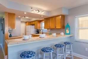 A modern kitchen with wooden cabinets, a central island with stools, and a window with blinds.