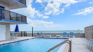 A pool area with a view of the ocean, a balcony with a railing, and lounge chairs. - Superb Location on the Beaches of Madeira. Great Corner Unit Views. Beachfront Pool on the Sand! (Madeira Beach)