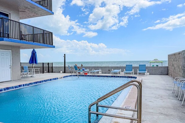 A pool area with a view of the ocean, a balcony with a railing, and lounge chairs. - Superb Location on the Beaches of Madeira. Great Corner Unit Views. Beachfront Pool on the Sand! (Madeira Beach)
