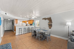 A spacious kitchen with a central island, a dining area with six chairs, and a living area with a sofa and a lamp.