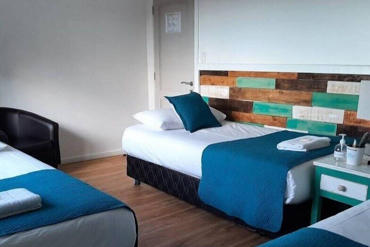 Ein Hotelzimmer mit zwei Betten, einem hölzernen Kopfteil, einem kleinen Tisch mit Flasche und Tasse sowie einem Sessel.