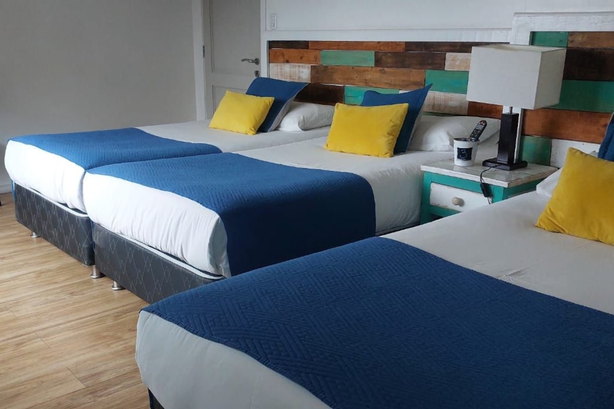 Une chambre d’hôtel avec trois lits, chacun doté d’une literie bleue et blanche, et d’une tête de lit en bois.
