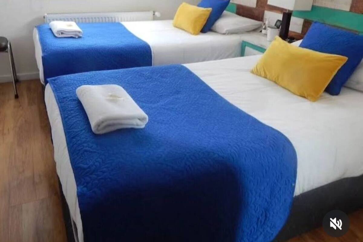 Ein Hotelzimmer mit zwei Betten, jeweils mit blau-weißer Bettwäsche und gelben Kissen.