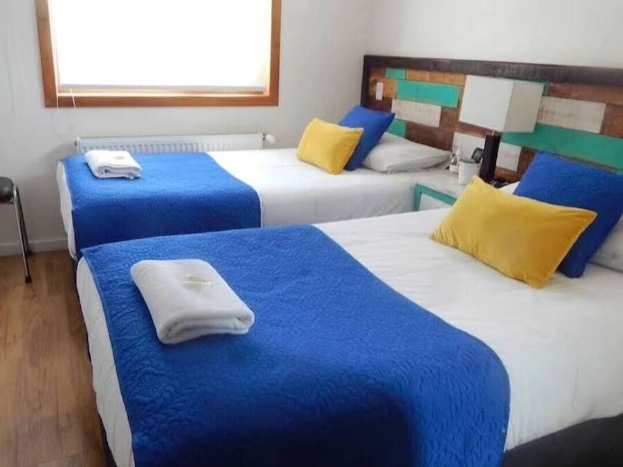 A hotel room with two beds, each with blue and white bedding and yellow pillows.