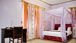 A bedroom with a four-poster bed, a desk with a chair, and patterned curtains. - Glory Summit Hotel (Hoima)