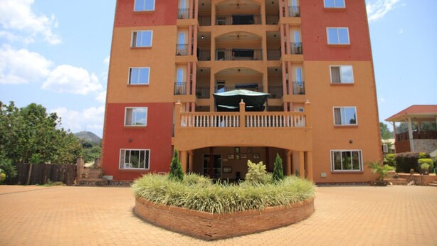 A multi-story building with balconies, a central entrance, and a landscaped area with plants. - Glory Summit Hotel (Hoima)