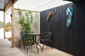 Een houten terras met twee zwarte metalen stoelen en een kleine ronde tafel.