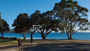 Een buitenbasketbalveld met een net, omringd door bomen en met uitzicht op een waterpartij.