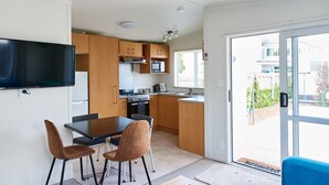 Een moderne keuken met houten kastjes, een flatscreen televisie en een eethoek met twee stoelen.