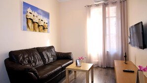 Een woonkamer met een bruine leren bank, een houten salontafel, een aan de muur bevestigde televisie, en een schilderij van een kasteel.