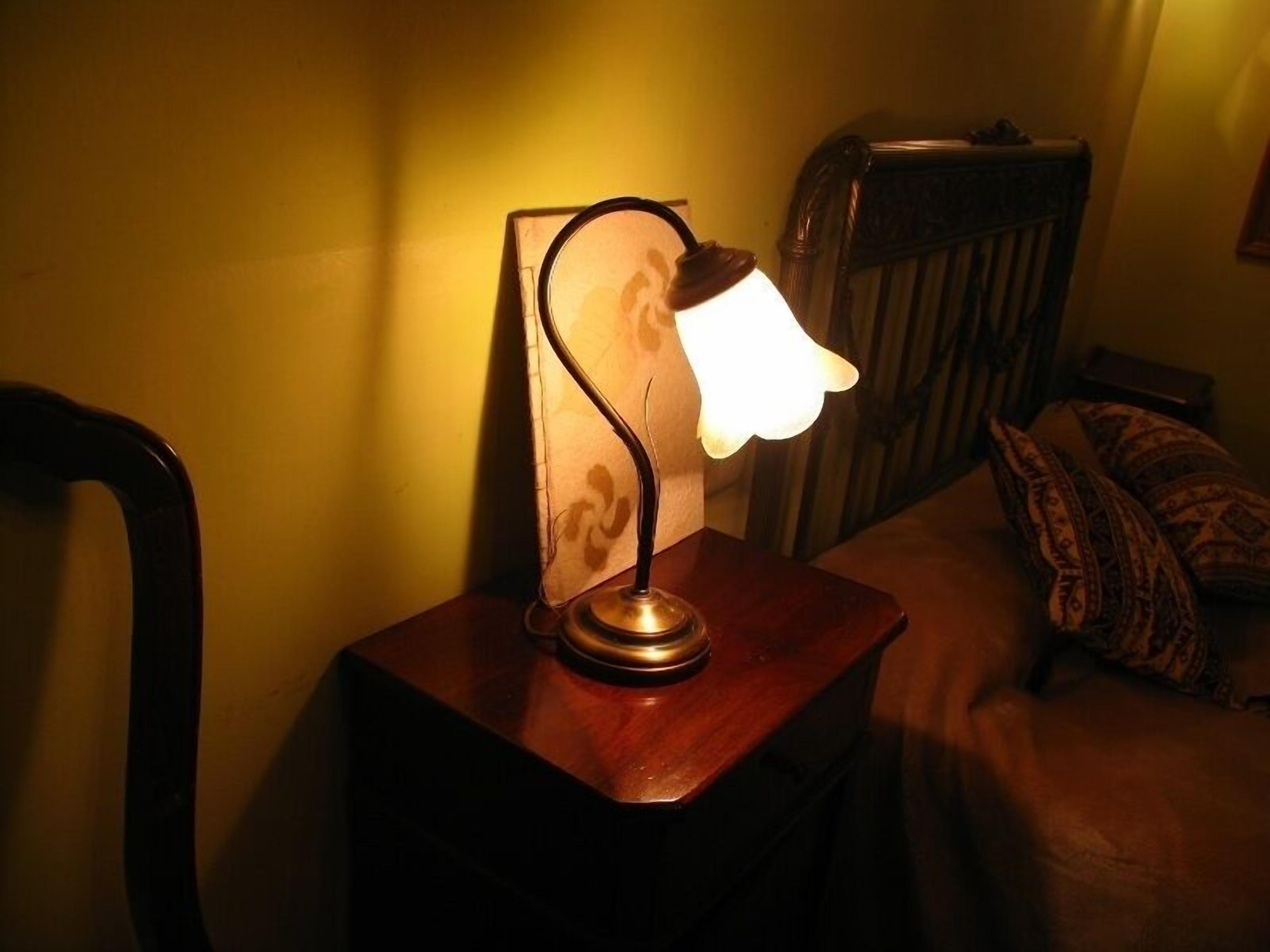 Une table de chevet avec une lampe, une chaise et un lit agrémenté d’oreillers à motifs.